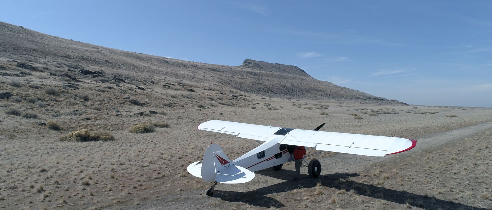 A white and red taildragger parked on desert flats below a mesa